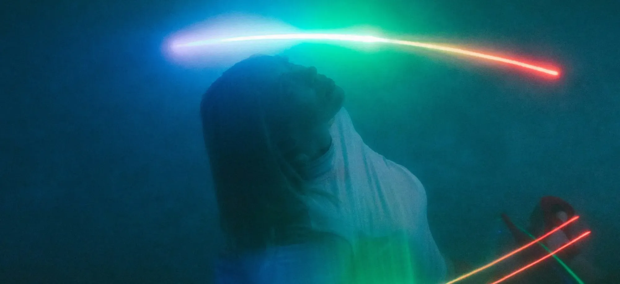 A silhouette of a woman leaning back, illuminated by vibrant streaks of blue, green, and red light, creating a dreamy, ethereal effect.