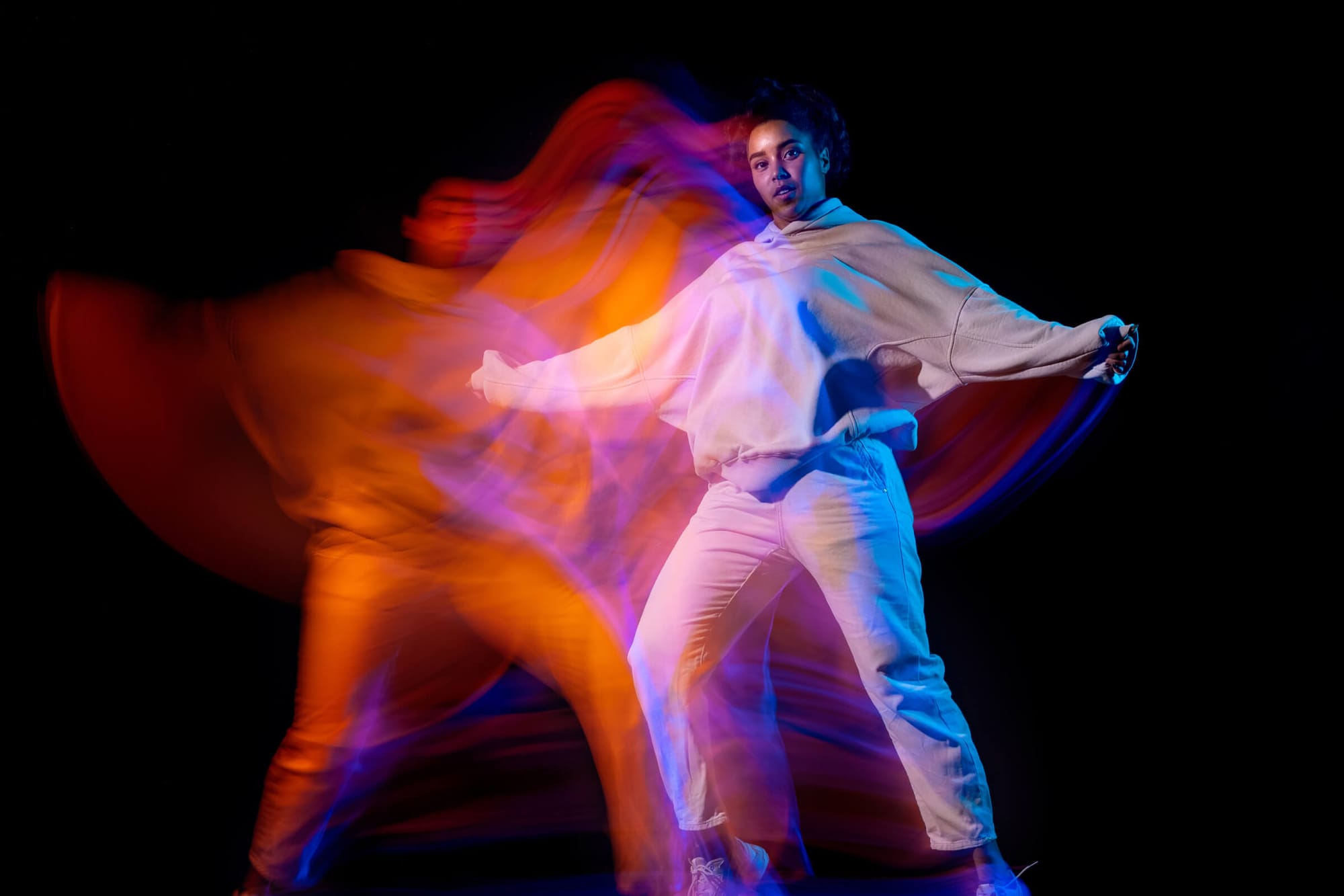 A person dancing with vibrant orange, purple, and blue light trails, creating dynamic motion and energy in the image.