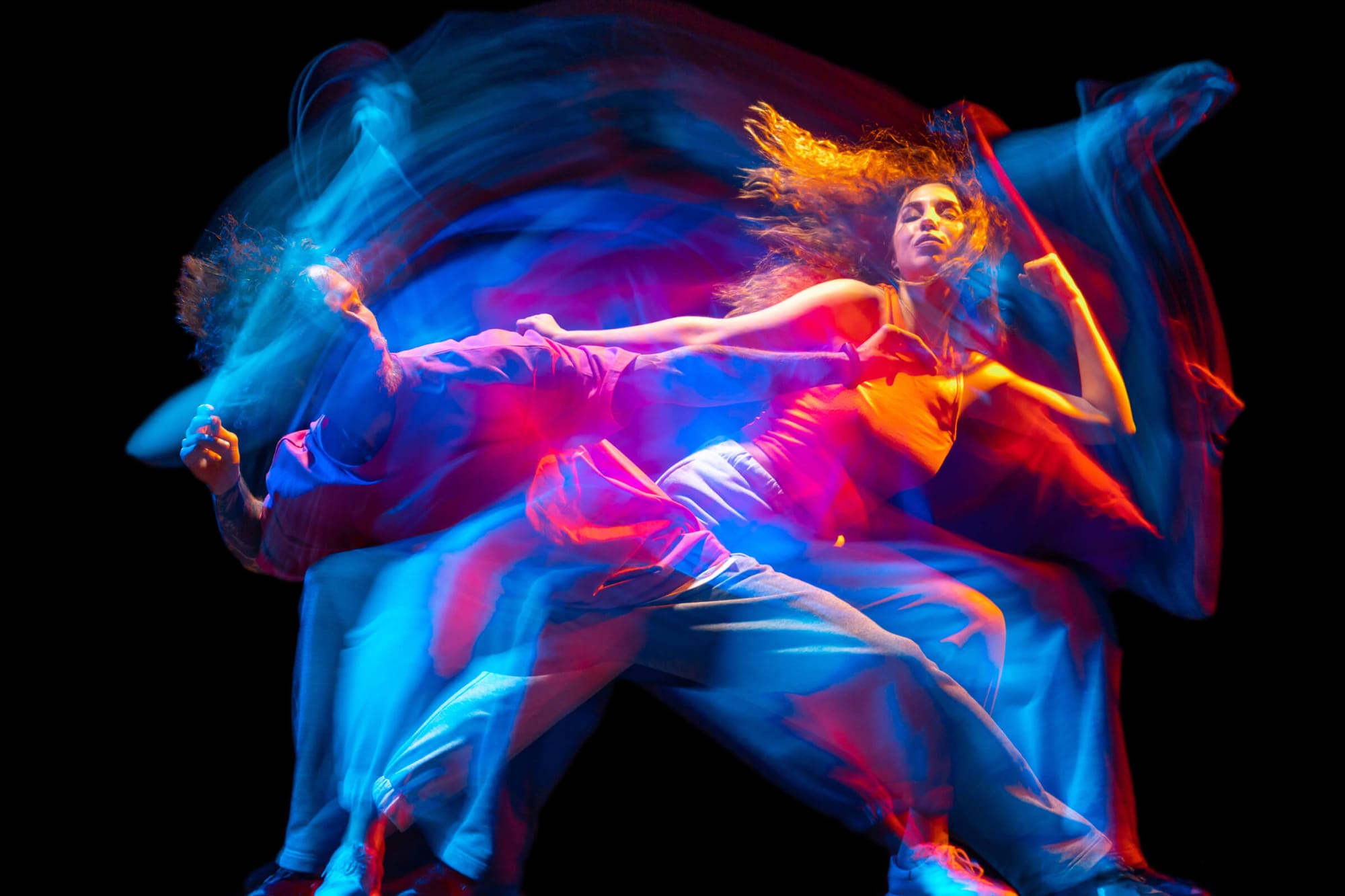 A dynamic image of two dancers in motion, with vibrant blue, red, and orange light trails creating an energetic and fluid effect.