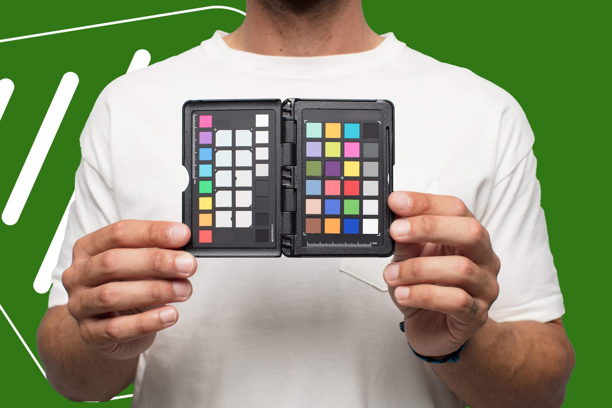 A person holding a color calibration chart with vibrant blocks against a green background.