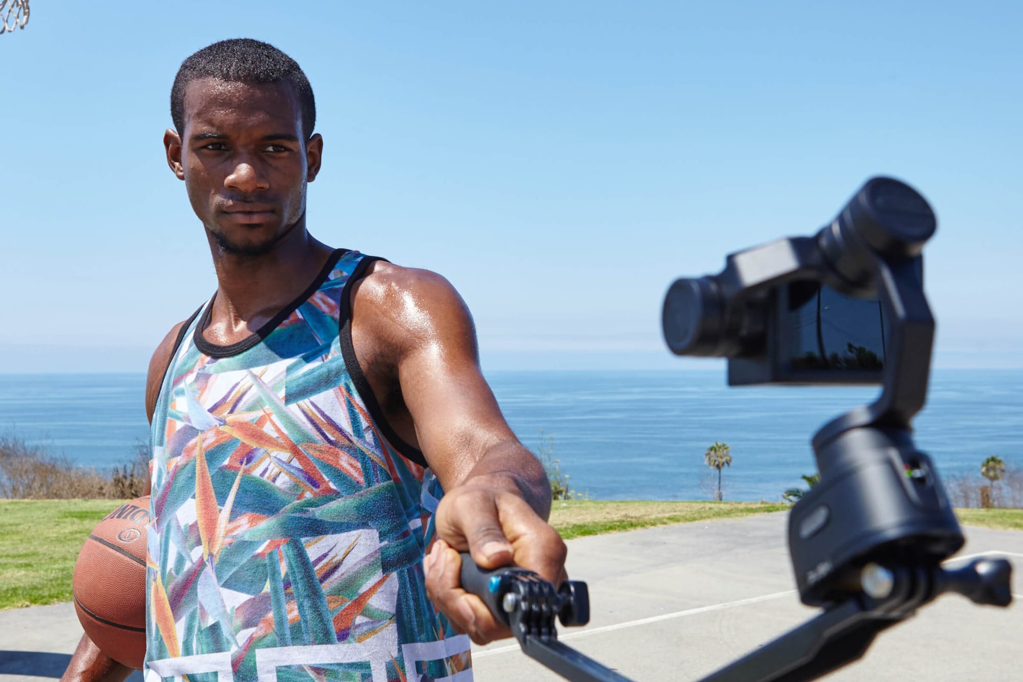 Man holding a gimbal while playing basketball near the ocean