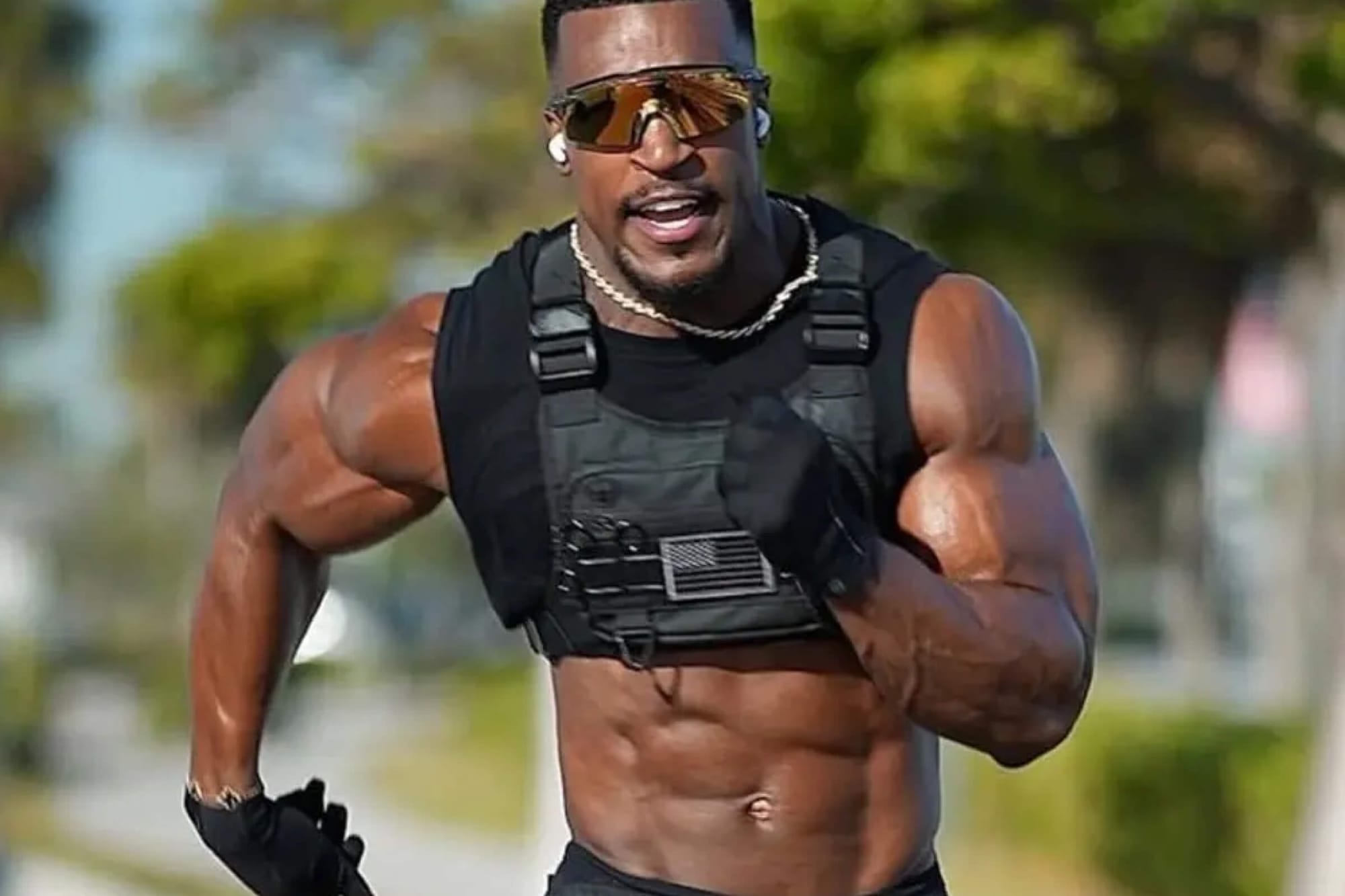 Ashton Hall running outdoors wearing a black weighted vest, sunglasses, and gloves.