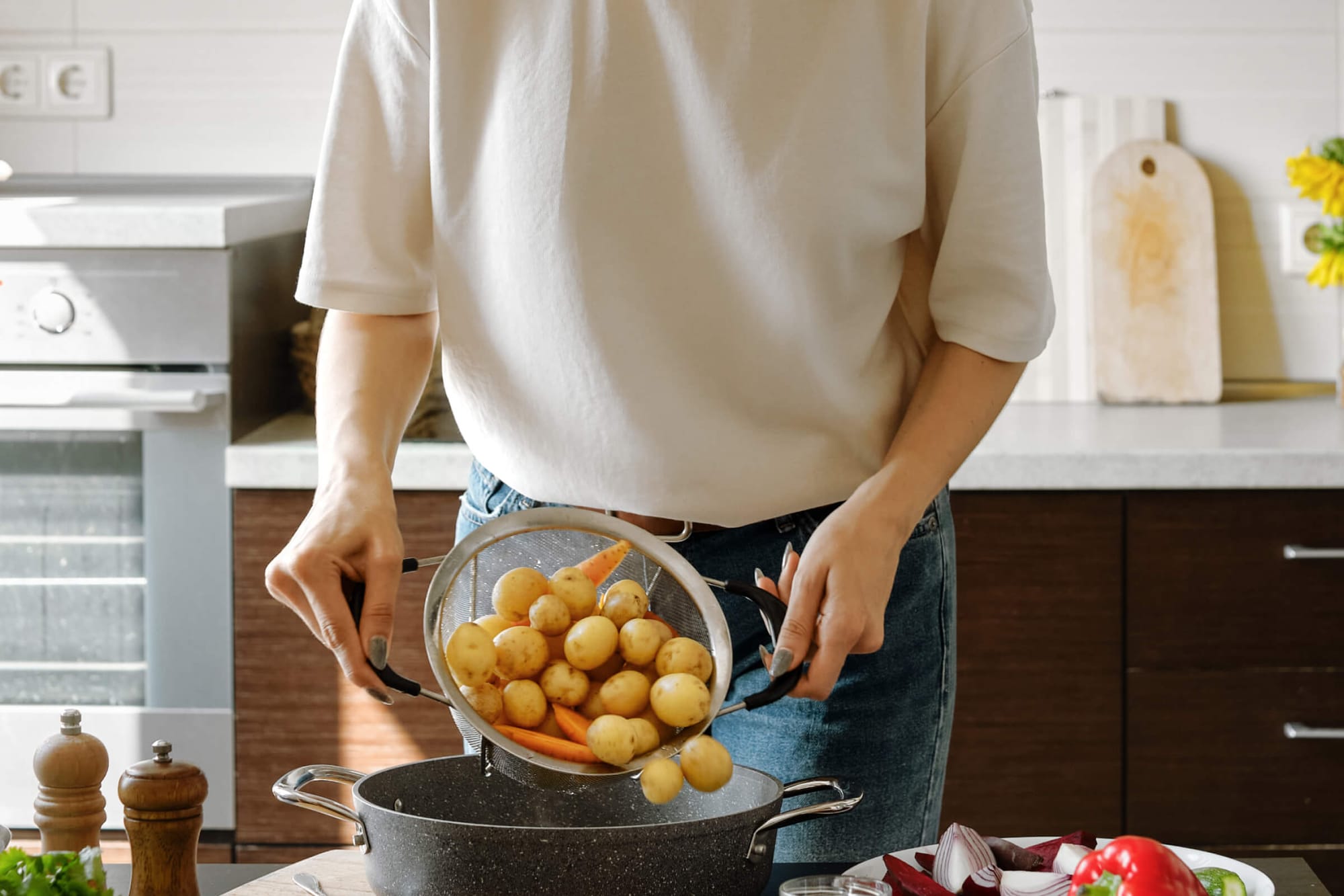 Person pouring baby potatoes and carrots into a pot in a kitchen.